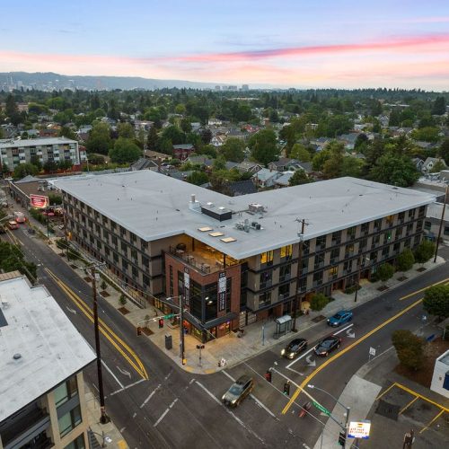 Aerial view of a modern, multi-story apartment building at a street intersection in a suburban neighborhood at sunset.